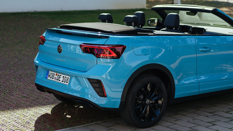 VW T-Roc Cabriolet R-Line in Hellblau mit offenem Verdeck auf einem Parkplatz, seitlicher Blick auf das Heck