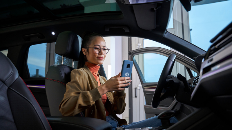 Eine Frau sitzt in einem VW Auto und schaut auf ihr Handy – Hilfe zu Apps und digitalen Diensten