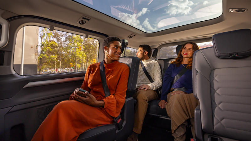 Drei Personen sitzen in einem VW Caravelle, der Blick geht durch das Panoramaglasdach nach außen.
