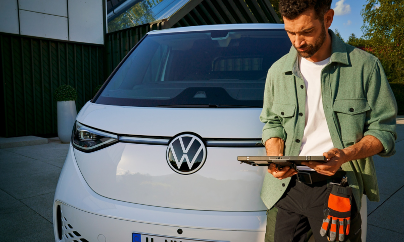 Un artisan se tient à côté d’un VW ID. Buzz Cargo et regarde une tablette.