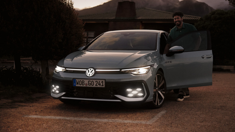 Un Volkswagen Golf GTE de color blanco de noche con los faros encendidos estacionado con la puerta del conductor abierta